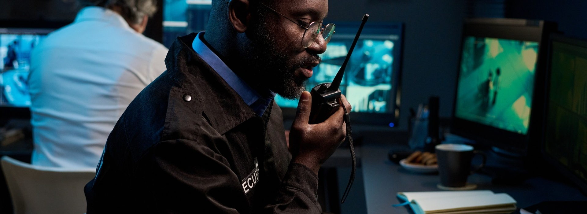 Security officer talking on a handheld two-way radio at a monitoring desk
