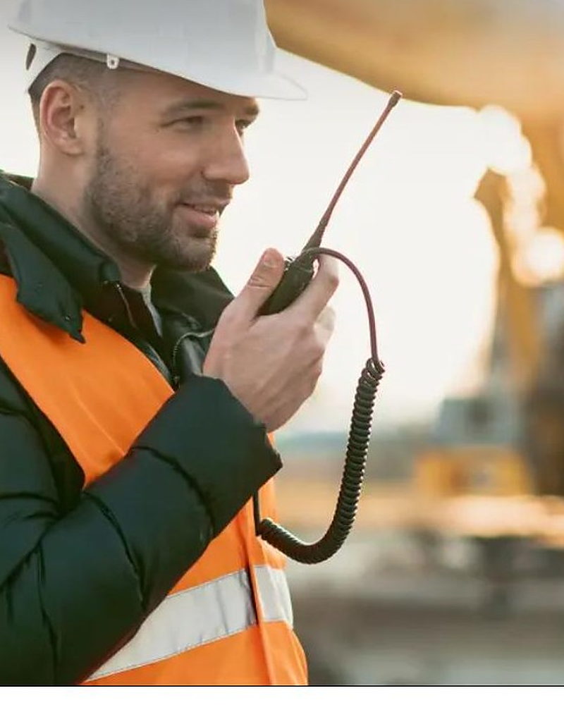 Site worker in hard hat and hi-vis talking on a two-way radio